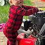 baby, barefoot, checkered_clothing, child, concrete, curious, footwear, garden, grass, lawn_mower, machine, outdoor, person, playful, red_onesie, standing, toddler, toy, wheel, young_child
