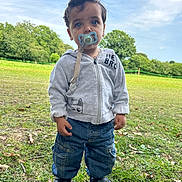 Rayan participe au concours pour gagner de l'argent avec cette photo : toddler, child, pacifier, hoodie, jeans, outdoor, grass, trees, sky, footwear, greenery, nature, casual_clothing, young_child, portrait, daylight, standing, expression, cute, park