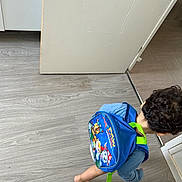 Rayan participe au concours pour gagner de l'argent avec cette photo : backpack, barefoot, blue, casual, child, clothing, curly, curly_hair, door, floor, indoor, kid, motion, paw_patrol, person, playful, room, toy, walking, young