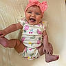baby, infant, smiling, happy, cute, onesie, headband, pink_bow, fruit_pattern, lying_down, blanket, skin, chubby_cheeks, playful, child, toddler, indoor, portrait, joyful, expression
