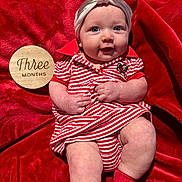 Maibel is registered to the contest to win money with this photo: baby, infant, child, red_blanket, striped_clothing, headband, bow, milestone_sign, wooden_sign, sitting, cute, smiling, portrait, indoor, soft_texture, sock, red, white, person, newborn