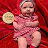 baby, infant, child, red_blanket, striped_clothing, headband, bow, milestone_sign, wooden_sign, sitting, cute, smiling, portrait, indoor, soft_texture, sock, red, white, person, newborn