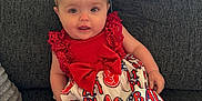 Kayleigh is registered to the contest to win money with this photo: baby, child, dress, headband, bow, couch, gray_couch, sitting, smiling, cute, infant, patterned_clothing, red_clothing, white_clothing, indoor, portrait, happy, person, young_child, comfortable