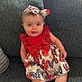 baby, child, dress, headband, bow, couch, gray_couch, sitting, smiling, cute, infant, patterned_clothing, red_clothing, white_clothing, indoor, portrait, happy, person, young_child, comfortable