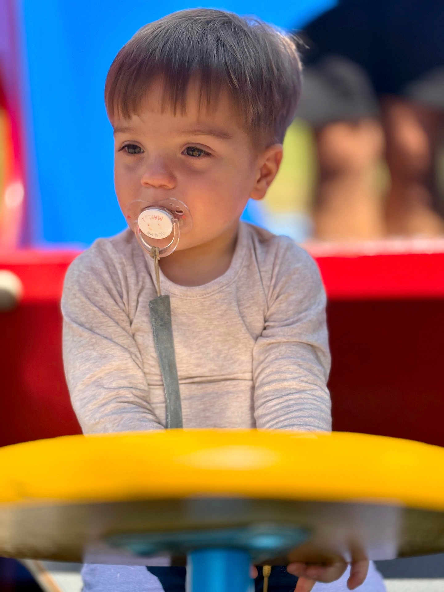 Ayden Vincent participe au concours pour gagner de l'argent avec cette photo : toddler, child, pacifier, playground, yellow, toy, outdoor, daylight, casual_clothing, curious, sitting, young_child, person, blurry_background, short_hair, cute, play, baby, infant, face