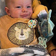 Nino a rejoint le concours — aidez-le/la à gagner de superbes lots ! baby, infant, smiling, face, blanket, plush_toy, pacifier, clothing, lion_design, onesie, cozy, child, cute, indoors, soft_texture, comfort, happy, young, resting, closeup