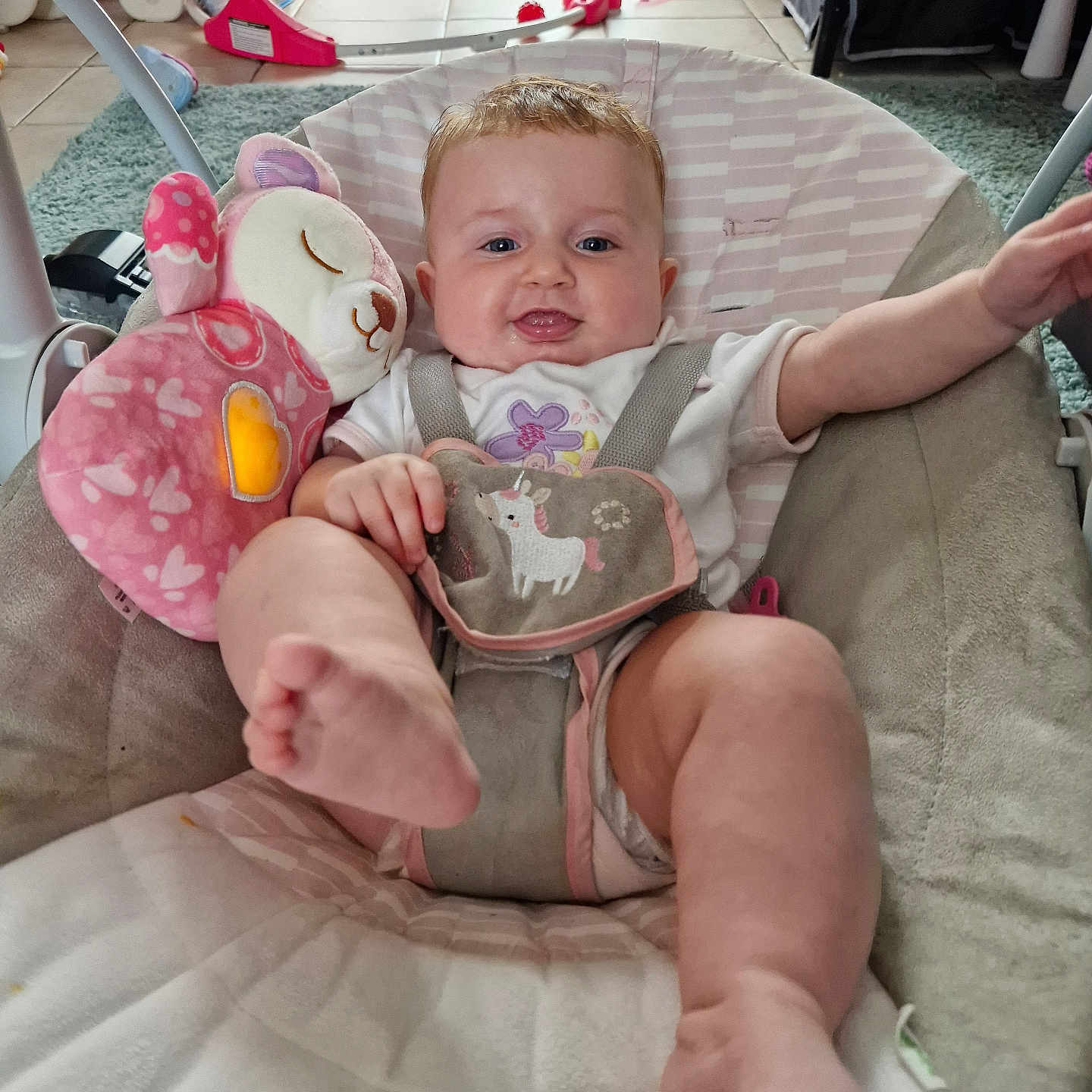 Rylee is registered to the contest to win money with this photo: arm_raised, baby, baby_seat, blanket, carpet, casual_clothing, child, childcare, cute, floor, happy, home, indoor, infant, kicking, person, pink_toy, plush_toy, smiling, soft_toy