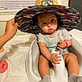 Mathew is registered to the contest to win money with this photo: baby, child, clothing, colorful_hat, cozy, curious, floor_seat, furniture, gray_shirt, hand, hat, indoor, light, person, playful, room, seat, socks, wide_eyes, window