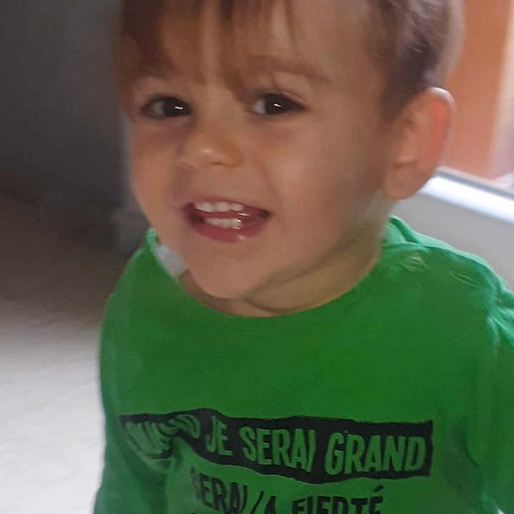 Kelyan participe au concours pour gagner de l'argent avec cette photo : background, casual_clothing, child, cute, expression, face, green_shirt, hair, happy, indoor, jeans, light, natural_light, person, portrait, smiling, standing, toddler, window, young_child