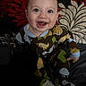 baby, child, smiling, dinosaur_onesie, sitting, indoor, happy, face, expression, pillow, pattern, floral, cute, infant, portrait, clothing, eyes, mouth_open, cheerful, young