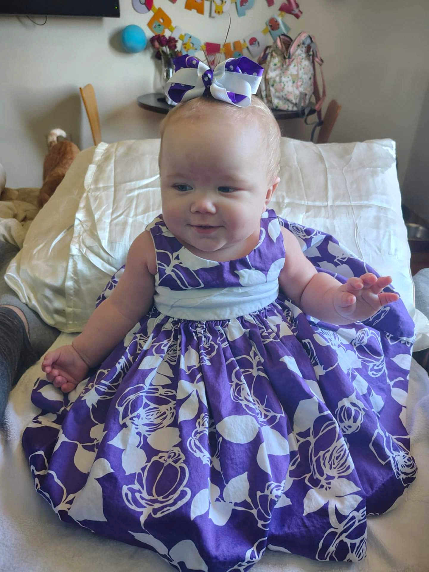 Kylynne Lorraine joined the competition — help win amazing prizes! baby, child, dress, purple_dress, bow, headband, pillow, bed, blanket, smile, cheeks, indoor, party_decorations, backpack, table, chair, person, portrait, hand, plush_toy