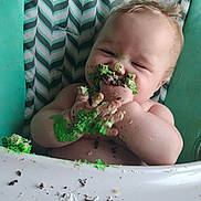 Kylynne Lorraine is registered to the contest to win money with this photo: baby, infant, highchair, cake, frosting, green_frosting, crumbs, messy, hands, face, smile, eating, tray, seat, cute, cheeks, happy, food, dessert, playful
