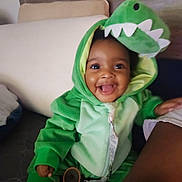 Danielle joined the competition — help win amazing prizes! baby, child, dinosaur_costume, green_clothing, smile, happy, indoor, cute, onesie, face, infant, seated, tongue_out, plush, hooded, cozy, portrait, playful, person, young_child