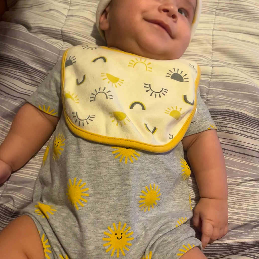Calixto is registered to the contest to win money with this photo: baby, bed, bedding, child, chubby, cute, face, grey, hand, happy, hat, infant, lying_down, onesie, pattern, skin, smiling, striped, sun, yellow