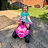Josefina-Ravenna joined the competition — help win amazing prizes! toddler, child, toy_vehicle, pink, minnie_mouse, outdoor, pavement, grass, brick_house, sunlight, smiling, curly_hair, blue_bow, play, fun, summer, daytime, happy, cute, person