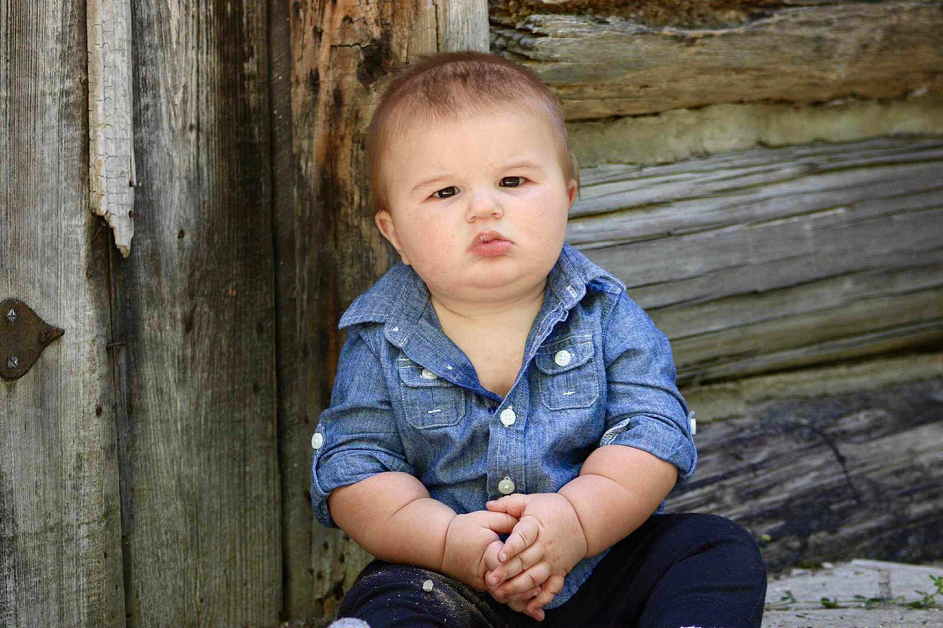 Carter joined the competition — help win amazing prizes! baby, child, denim_shirt, sitting, hands_clasped, serious_expression, wooden_wall, outdoor, portrait, candid, casual_clothing, chubby_arms, short_hair, natural_light, texture, rustic, young, person, cute, face