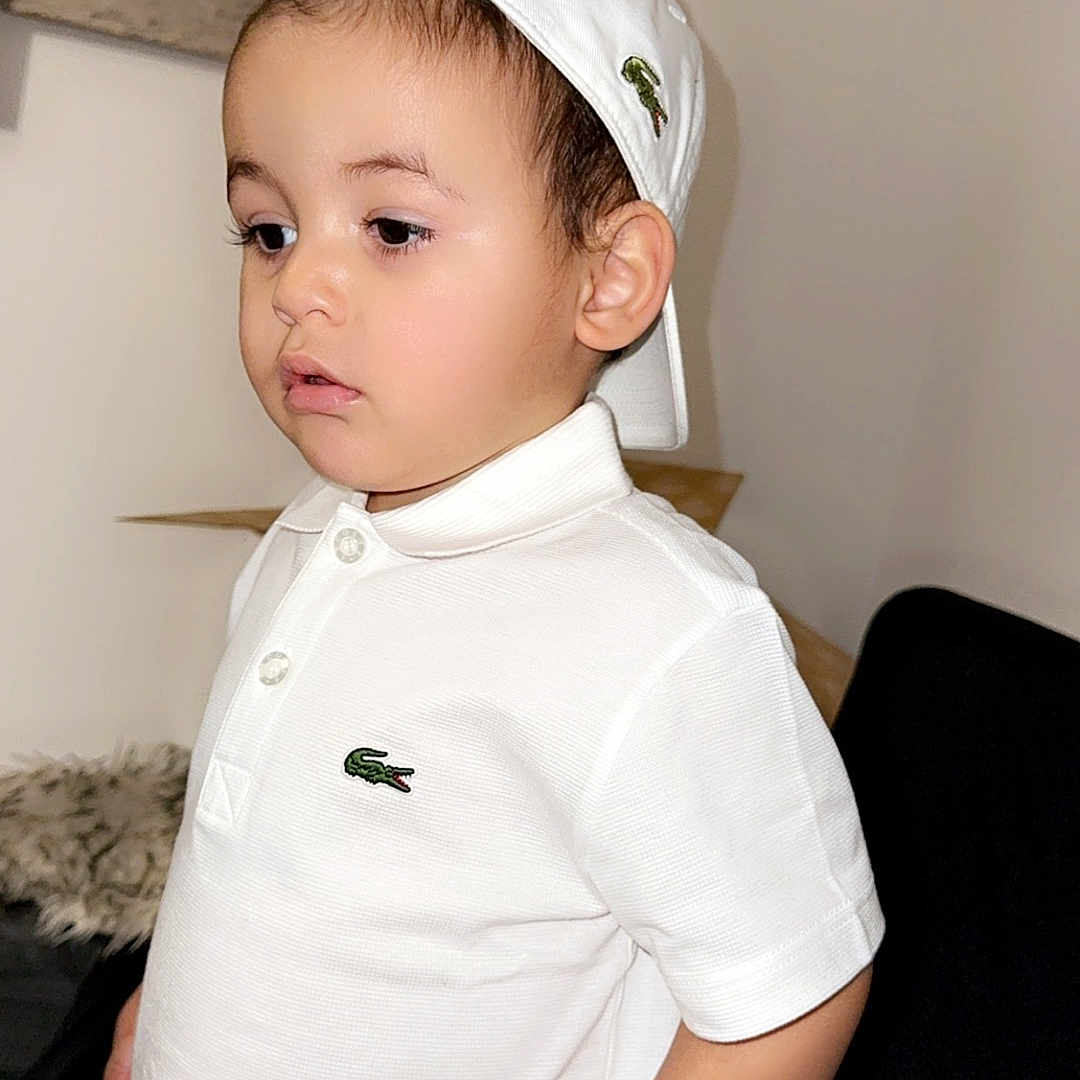 Chahine participe au concours pour gagner de l'argent avec cette photo : accessories, baby, baseballcap, bodypart, cap, clothing, couch, dress, face, finger, furniture, hand, hat, head, person, photography, portrait, shirt, sleeve, t_shirt