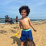 Rakim joined the competition — help win amazing prizes! child, beach, sand, ocean, waves, sunlight, curly_hair, toddler, yellow_shovel, blue_shorts, sky, people, summer, vacation, outdoor, play, fun, barefoot, water, family