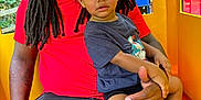 Amarion joined the competition — help win amazing prizes! child, adult, man, toddler, dreadlocks, cap, red_shirt, blue_tshirt, playground, play_structure, yellow, blue, orange, outdoor, greenery, seated, holding, curious, casual_clothing, family