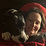 Bill is registered to the contest to win money with this photo: woman, dog, pet, snuggling, cozy, red_blanket, indoor, portrait, black_and_white_dog, resting, closeup, casual, warm_lighting, comfort, affection, relaxation, home, companion, animal, friendship