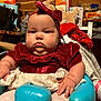 baby, child, infant, red_dress, headband, blue_seat, indoor, cute, chubby_cheeks, portrait, furniture, clothing, holiday_outfit, tights, hand, face, expressionless, household_items, background, plush_toy