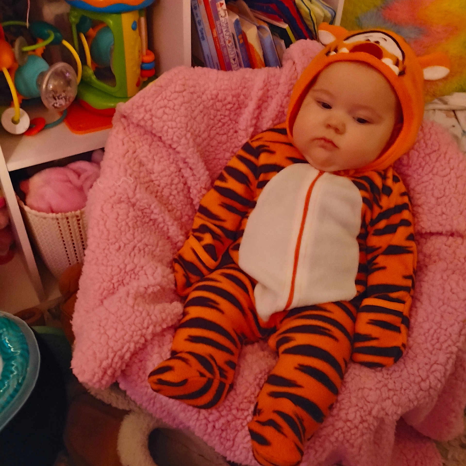 Novella is registered to the contest to win money with this photo: baby, books, child, colorful, cozy, cute, expression, headwear, indoor, infant, onesie, patterned_clothing, person, pink_blanket, plush, resting, seat, soft, tiger_costume, toy