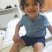 Mohamed Khorchi participe au concours pour gagner de l'argent avec cette photo : toddler, child, smiling, curly_hair, blue_shirt, navy_shorts, sandal, indoor, bed, white_bedspread, wooden_cabinet, heater, shoes, happy, portrait, person, casual_clothing, playful, floor, home