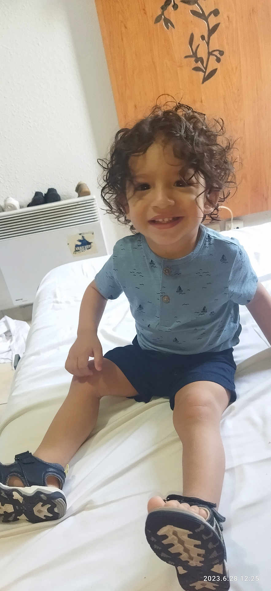 Mohamed Khorchi participe au concours pour gagner de l'argent avec cette photo : toddler, child, smiling, curly_hair, blue_shirt, navy_shorts, sandal, indoor, bed, white_bedspread, wooden_cabinet, heater, shoes, happy, portrait, person, casual_clothing, playful, floor, home