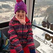Maëline participe au concours pour gagner de l'argent avec cette photo : child, girl, winter_clothing, beanie, pompom_hat, jacket, mittens, snow, gondola, ski_resort, window, mountains, village, smiling, portrait, travel, cold_weather, seat, colorful_pattern, scenic_view