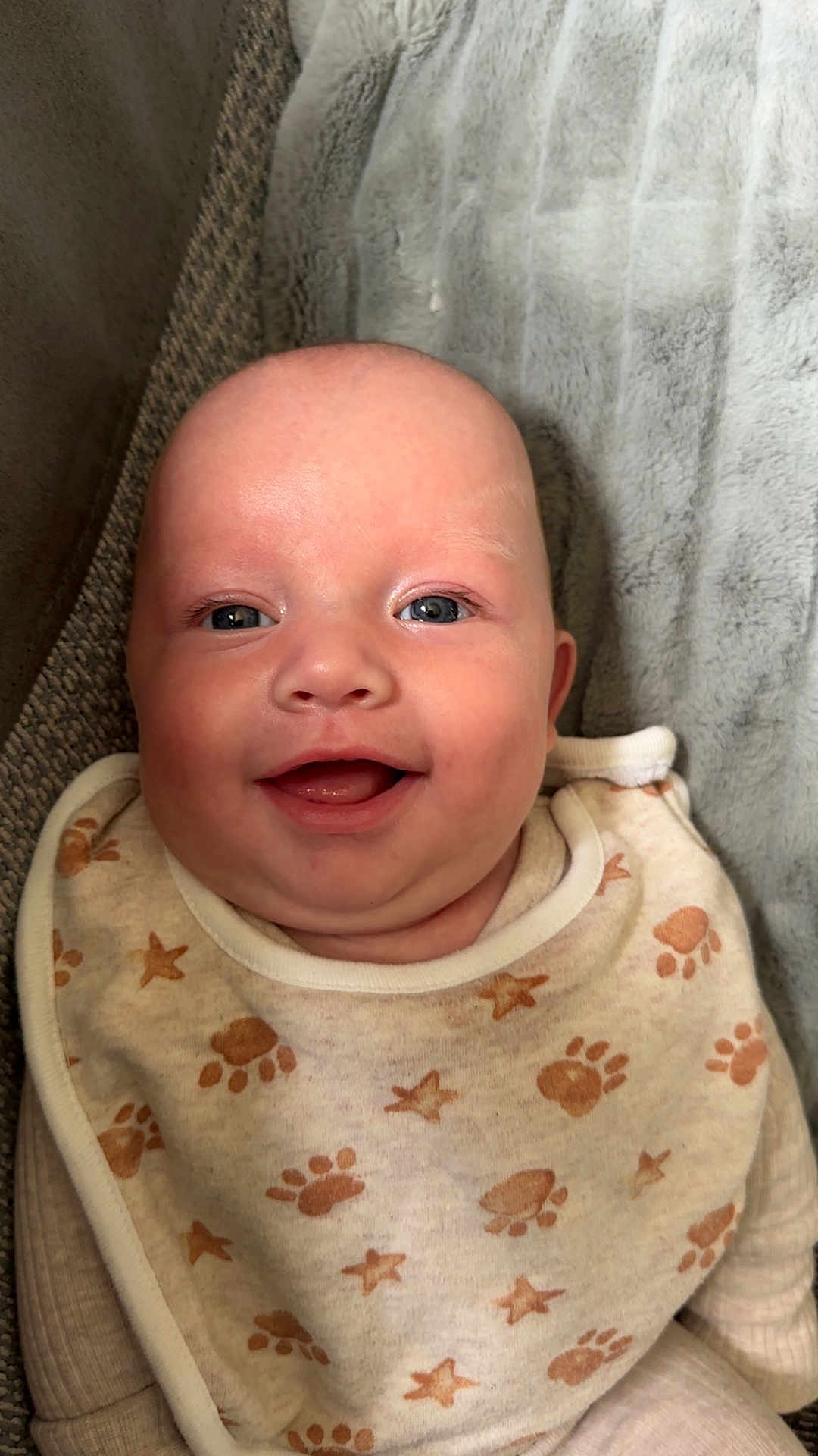 Archie-Lee-pattison is registered to the contest to win money with this photo: baby, smiling, face, bib, paw_prints, stars, blanket, infant, cute, happy, clothing, texture, closeup, portrait, child, soft, cozy, lying_down, skin, expression