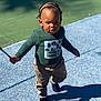 Rocket is registered to the contest to win money with this photo: toddler, child, outdoor, walking, sunlight, shadow, cornrows, stick, green_shirt, beige_pants, footwear, playground, texture, confident, determined, person, young_child, daylight, casual_clothing, nature