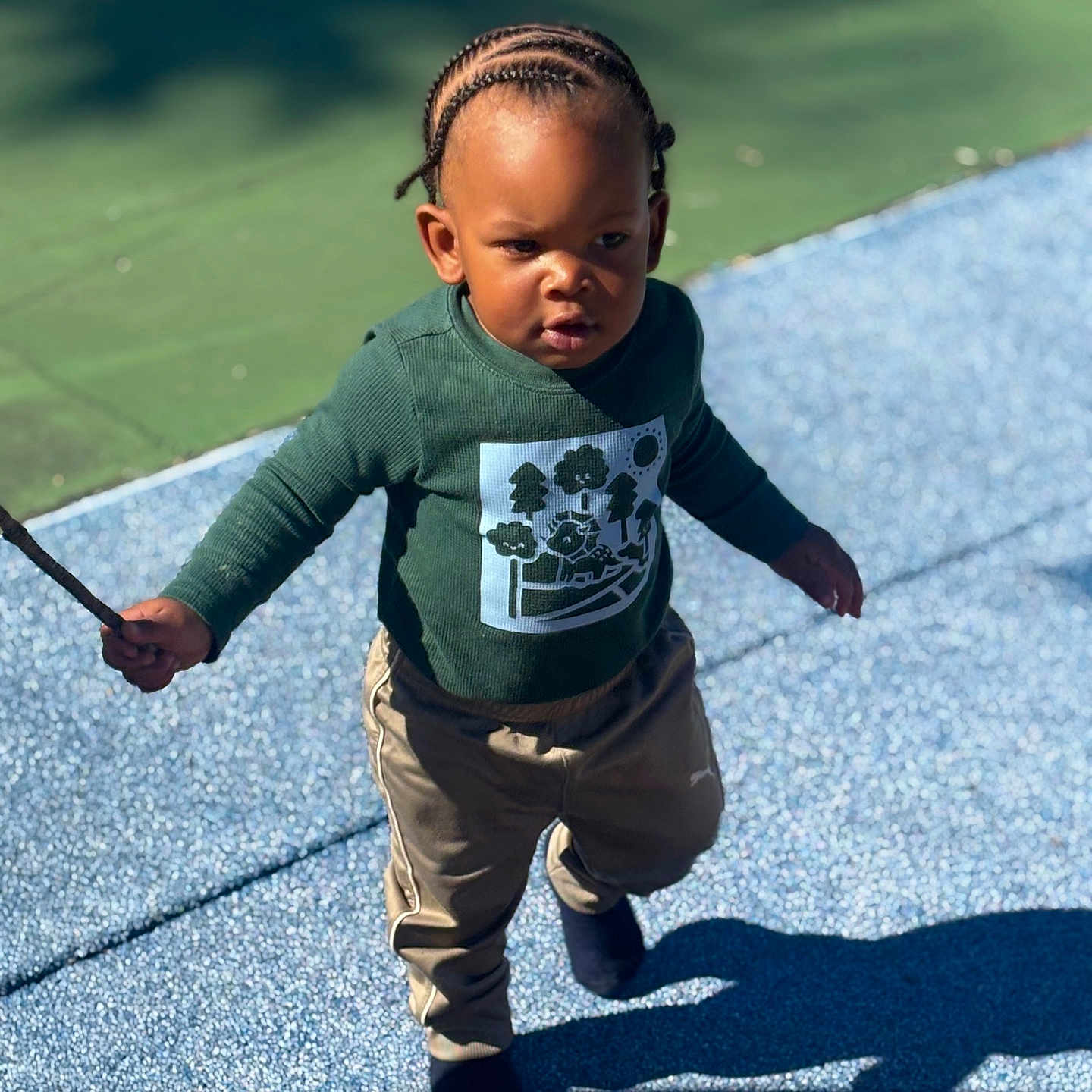 Rocket joined the competition — help win amazing prizes! beige_pants, casual_clothing, child, confident, cornrows, daylight, determined, footwear, green_shirt, nature, outdoor, person, playground, shadow, stick, sunlight, texture, toddler, walking, young_child