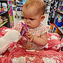 baby, child, shopping_cart, toy, plush, unicorn, teething_ring, store, shelf, shopping, pink, floral_dress, infant, girl, cute, indoor, retail, curious, person, cart