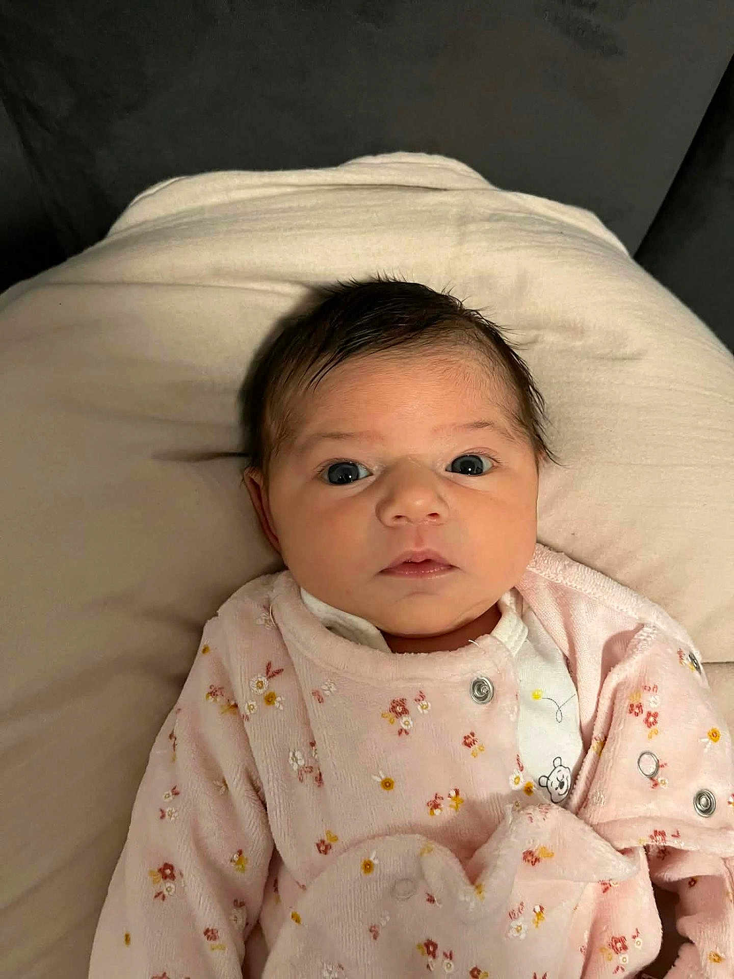 Cassandre a rejoint le concours — aidez-le/la à gagner de superbes lots ! baby, infant, face, clothing, onesie, pink, floral, pillow, soft, cute, newborn, portrait, indoors, resting, expression, curious, child, person, young, sleepwear