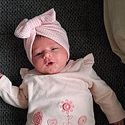 Rachel a rejoint le concours — aidez-le/la à gagner de superbes lots ! baby, infant, pink_clothing, headwrap, bow, lying_down, cute, soft_texture, face, child, apparel, socks, pattern, fabric, portrait, young, indoor, person, expression, resting
