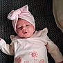 baby, infant, pink_clothing, headwrap, bow, lying_down, cute, soft_texture, face, child, apparel, socks, pattern, fabric, portrait, young, indoor, person, expression, resting