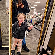 Raelynn is registered to the contest to win money with this photo: child, adult, mirror, store, aisle, jacket, pants, sneakers, smile, curly_hair, phone, reflection, carpet, shelf, product, lighting, casual, gesture, happy, shopping