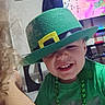 Jaxon is registered to the contest to win money with this photo: child, smiling, green_hat, green_shirt, indoor, television, face, dirt, necklace, happy, cute, boy, costume, party, playful, room, furniture, screen, closeup, fun