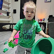 Jaxon is registered to the contest to win money with this photo: toddler, child, green_clothing, hat, shamrock, st_patricks_day, barefoot, indoor, living_room, floor, curtain, shelf, toy, person, portrait, smile, decor, holiday, celebration, young_child