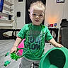 toddler, child, green_clothing, hat, shamrock, st_patricks_day, barefoot, indoor, living_room, floor, curtain, shelf, toy, person, portrait, smile, decor, holiday, celebration, young_child
