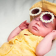 Ruby is registered to the contest to win money with this photo: baby, sleeping, yellow_clothing, hat, sunglasses, flower_frame, blanket, soft_texture, peaceful, infant, cute, portrait, relaxation, child, headwear, resting, skin, hand, closeup, comfort