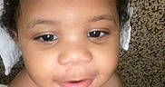 Dj is registered to the contest to win money with this photo: baby, child, infant, face, portrait, close_up, looking_at_camera, curious, serious_expression, open_mouth, bow, white_bow, blanket, carpet, indoor, home, sitting, bare_shoulders, head, photography