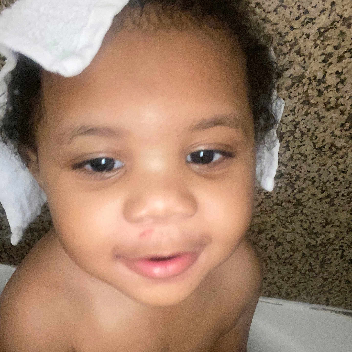 Dj is registered to the contest to win money with this photo: baby, child, infant, face, portrait, close_up, looking_at_camera, curious, serious_expression, open_mouth, bow, white_bow, blanket, carpet, indoor, home, sitting, bare_shoulders, head, photography