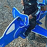 child, toddler, playground, spring_rider, ride_on_toy, outdoor, playground_equipment, blue, black_clothing, nike, sitting, serious_expression, adult, parent, wood_chips, recreation, park, sneaker, portrait, daylight