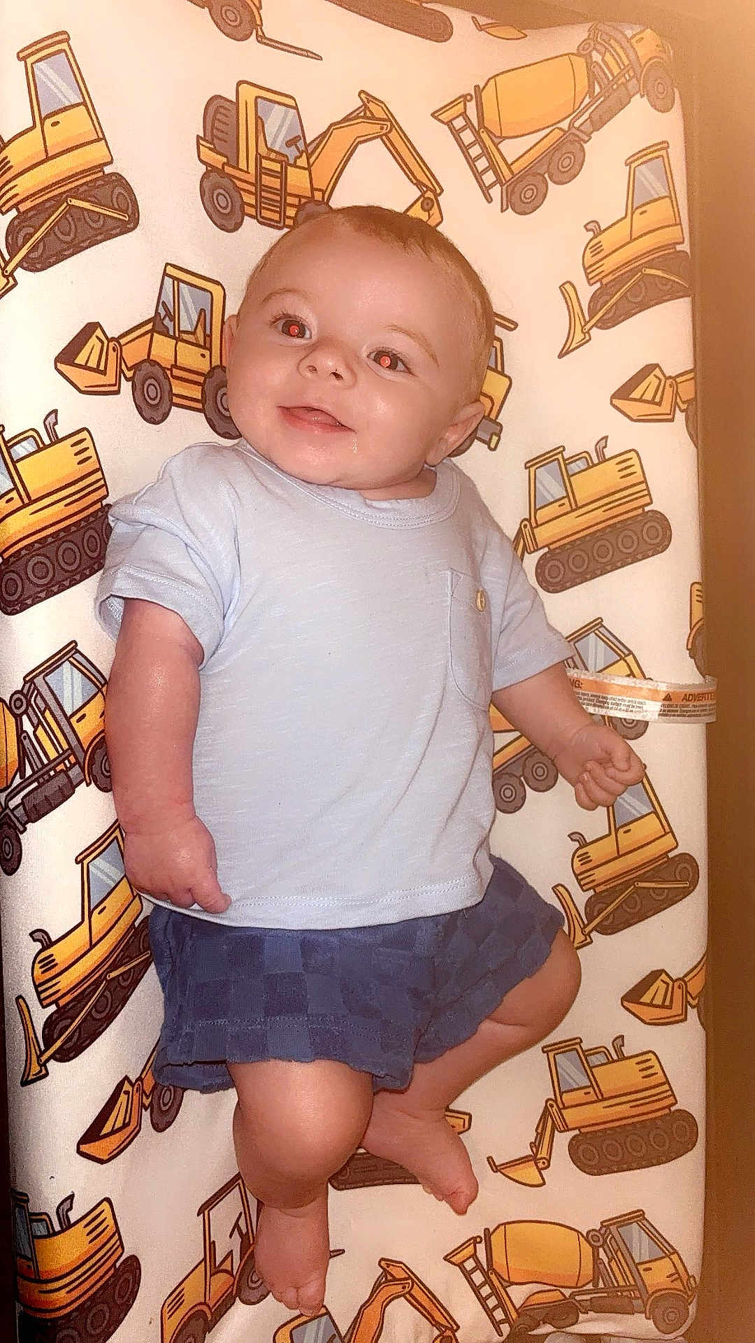 Knox joined the competition — help win amazing prizes! baby, child, smiling, blue_shirt, shorts, cushion, construction_vehicle_pattern, indoors, cheerful, drool, face, legs, feet, person, infant, cute, happy, pattern, toy_theme, background