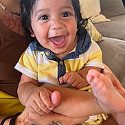 Fabian is registered to the contest to win money with this photo: baby, smiling, child, happy, face, hand, foot, tattoo, person, couch, indoor, clothing, yellow, blue, skin, portrait, holding, infant, casual, cute