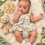 Srijita Barua joined the competition — help win amazing prizes! baby, infant, child, three_months, portrait, lying_down, smiling, floral_dress, dress, teddy_bear, blanket, flowers, daisies, greenery, wooden_sign, milestone_photo, nursery, cozy, socks, indoor