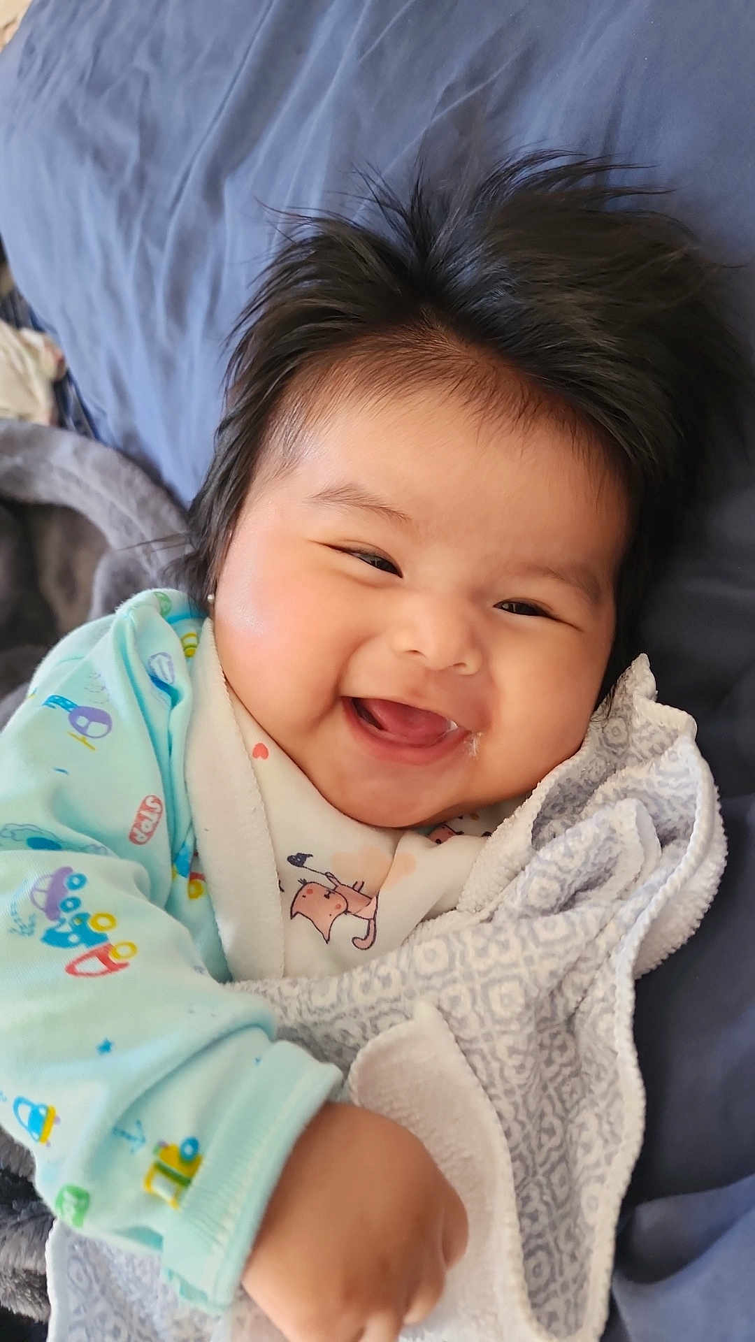 Aitana Aliz is registered to the contest to win money with this photo: baby, smiling, happy, blanket, onesie, infant, cute, child, face, hair, lying_down, cozy, patterned_blanket, soft_texture, indoors, portrait, cheerful, young_child, skin, hand