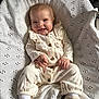 baby, smiling, onesie, knitted_blanket, shoes, white, cream, floral_pattern, happy, cute, infant, sitting, portrait, cozy, indoors, child, small_hands, soft_texture, clothing, fabric