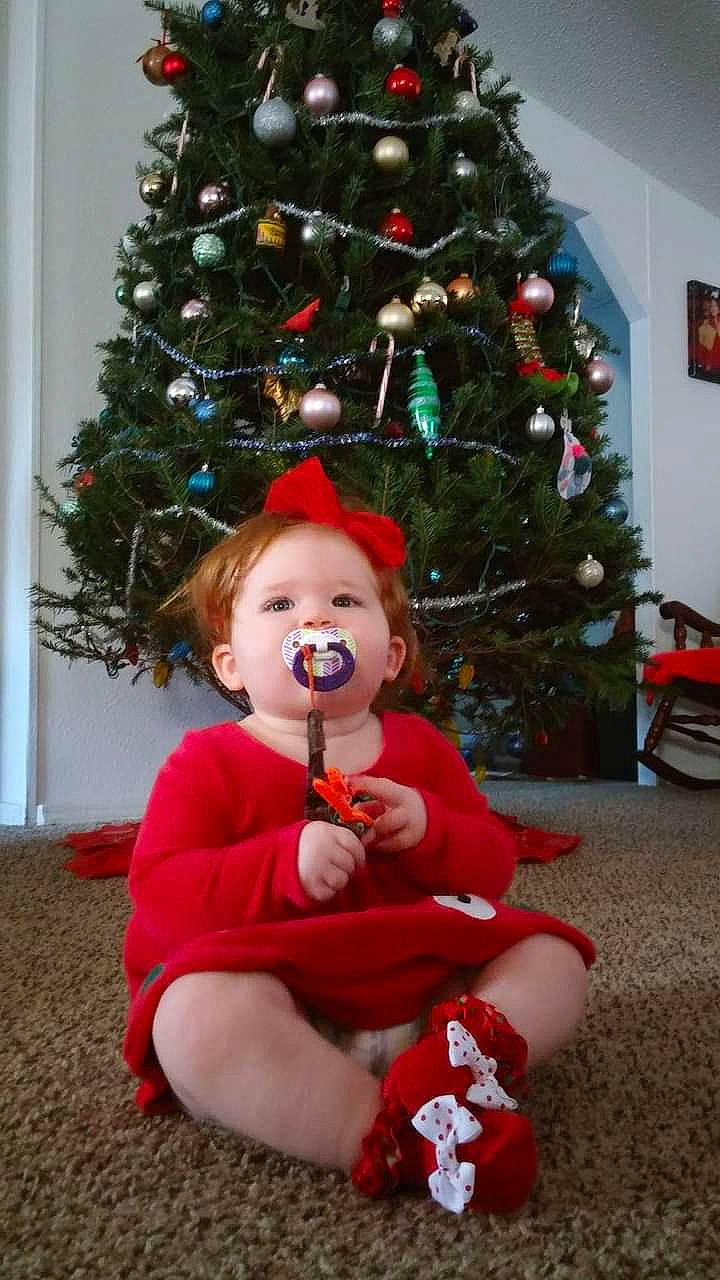 Rebecca is registered to the contest to win money with this photo: christmas, christmas_decoration, christmas_eve, christmas_ornament, christmas_tree, conifer, event, evergreen, happy, holiday, holiday_ornament, interior_design, lap, ornament, person, plant, red, standing, toddler, toy